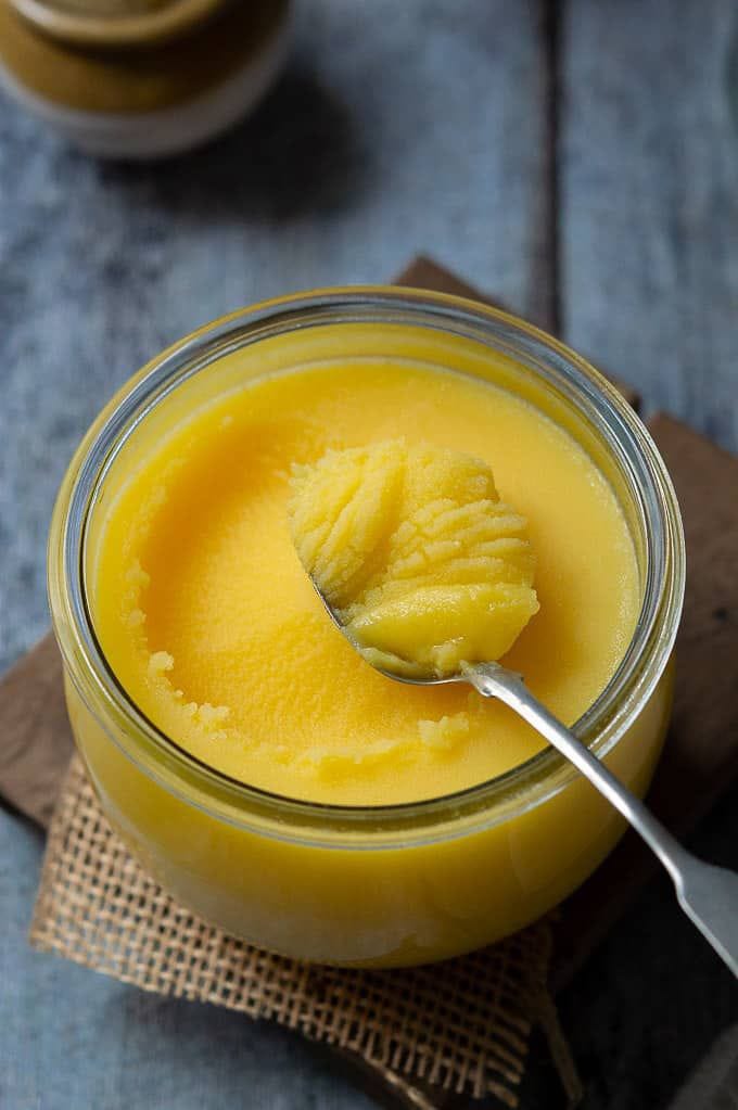 Spoonful of grainy danedar desi cow ghee lifted from an open jar khaas honey